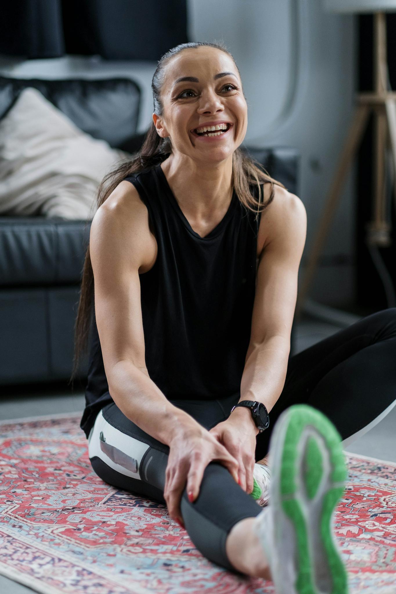 Smiling woman stretching on a rug indoors, promoting a healthy lifestyle.